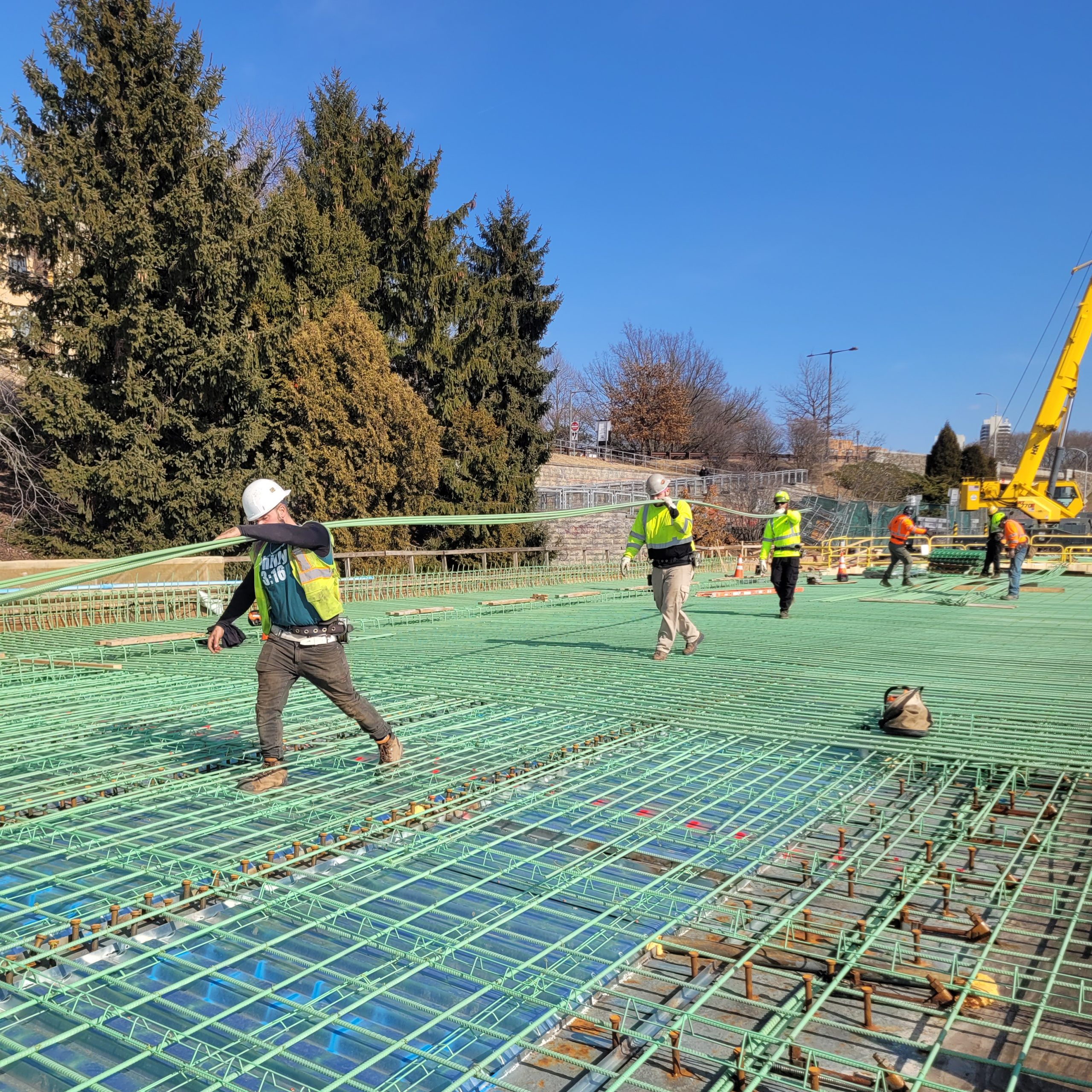 Workers carrying long lengths of rebar by hand across a construction deck